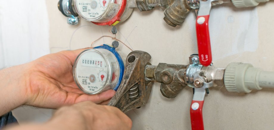 Male plumber fixing water meter with adjustable wrench.