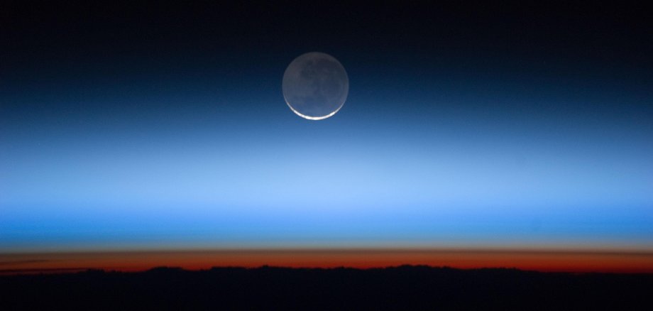 Blick von der Internationalen Raumstation (ISS) auf die Erde, im Hintergrund der Mond: Die einzelnen Schichten der Atmosphäre sind durch unterschiedliche Einfärbungen vorneinander zu unterscheiden: Troposphäre (orange), Tropospause (braun), Stratosphäre (grau). Die oberen Schichten, Mesosphäre, Thermosphäre und Exosphäre (blau bis schwarz). https://www.eskp.de/grundlagen/schadstoffe/atmosphaere-der-erde/
