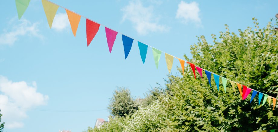 City festival event in park, street decorated with colorful triangular flags on sunny summer day against sky