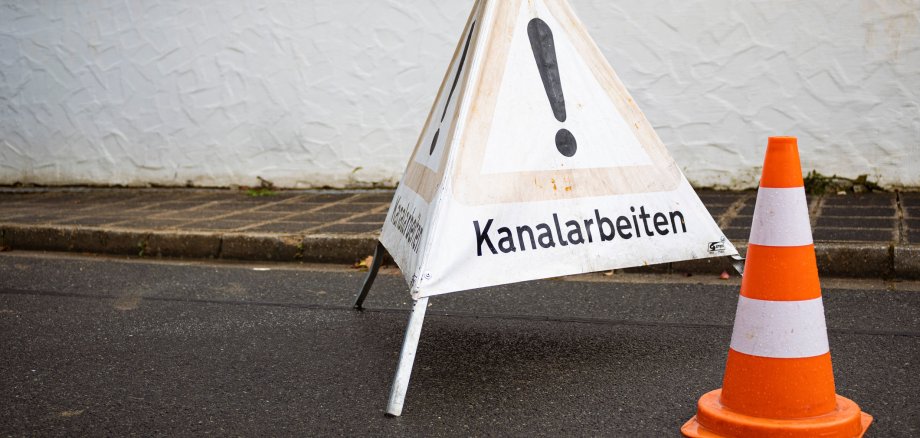 Warning sign and a traffic cone on the street
translation: Sewer works