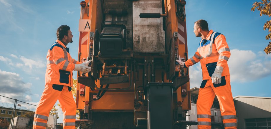 Two refuse collection workers loading garbage into waste truck