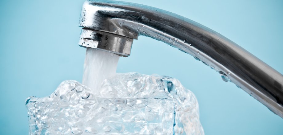 Close-up of water faucet pouring into overflowing glass